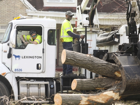 workers use a knuckleboom truck to lift large pieces of tree debris 