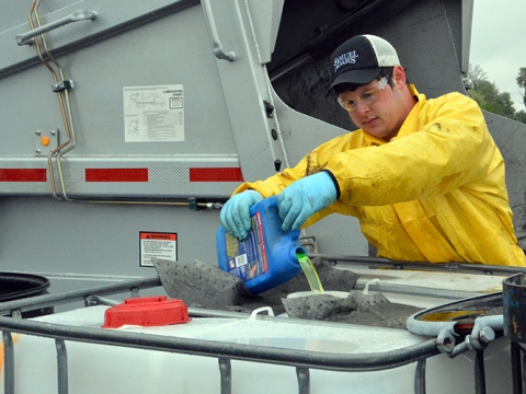 a worker pouring some kind of oil into a container with a truck behind him