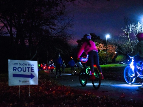 a sign that says "glow ride" and several bikes with lights on their tires in the background at night