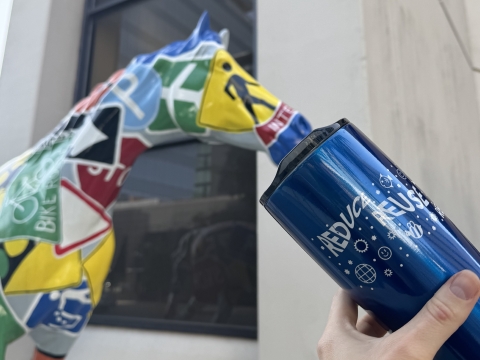 a blue reusable water bottle that says "reduce reuse" in front of a colorful horse statue 