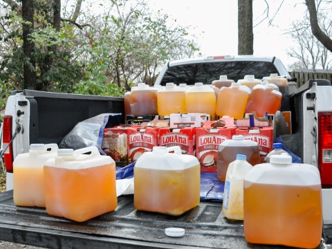 a truck bed outdoors with dozens of 5 gallon jugs of cooking oil stacked in it