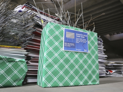 a green box that says "yard sign collection" with stakes and signs sticking out of it; there are more signs stacked in the background